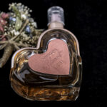 Heart-shaped perfume bottle with dried flowers on black background