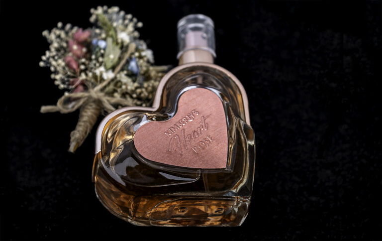 Heart-shaped perfume bottle with dried flowers on black background