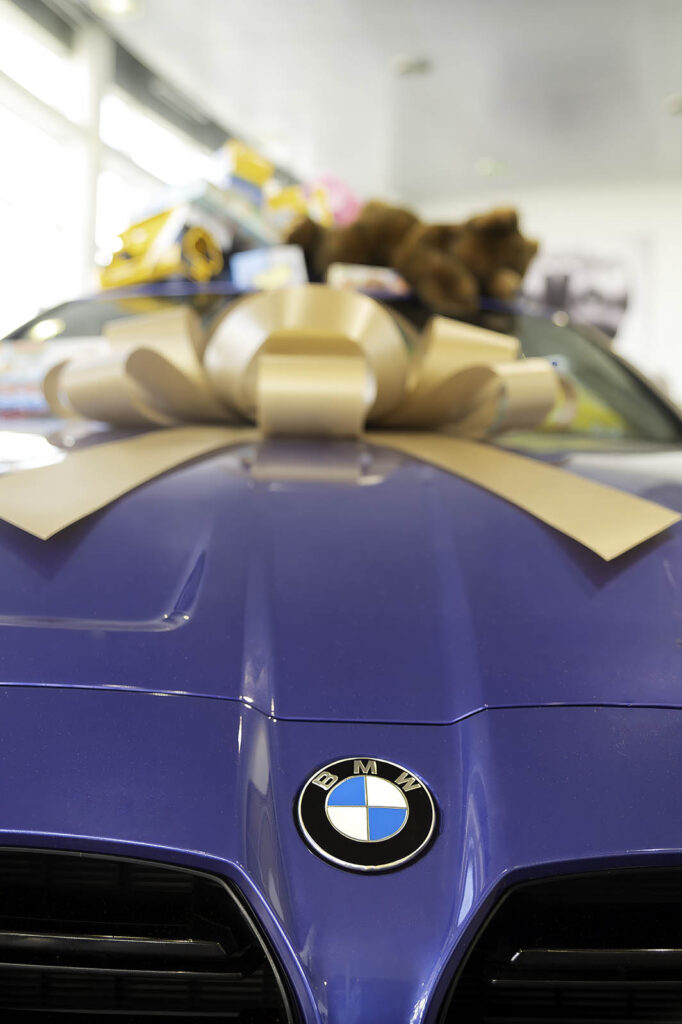 Blue BMW car hood with gold ribbon bow and brand logo in showroom setting