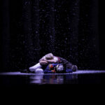 Theatrical performer on stage surrounded by falling snow effect with dramatic lighting