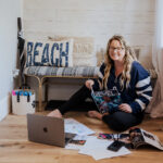 Woman sitting on floor with laptop and magazines in bright coastal-themed workspace
