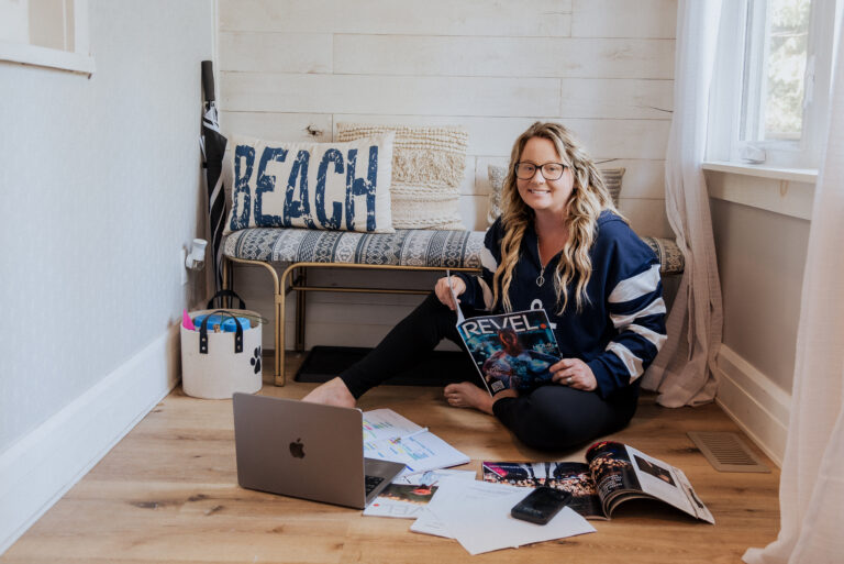 Woman sitting on floor with laptop and magazines in bright coastal-themed workspace