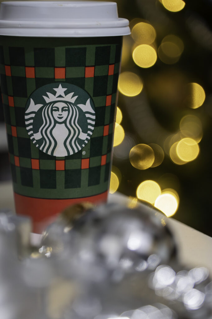 Festive plaid starbucks coffee cup with golden bokeh lights in holiday setting