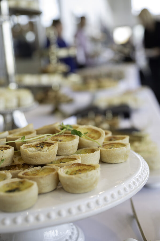 Elegant mini quiches garnished with microgreens on white serving platter at event